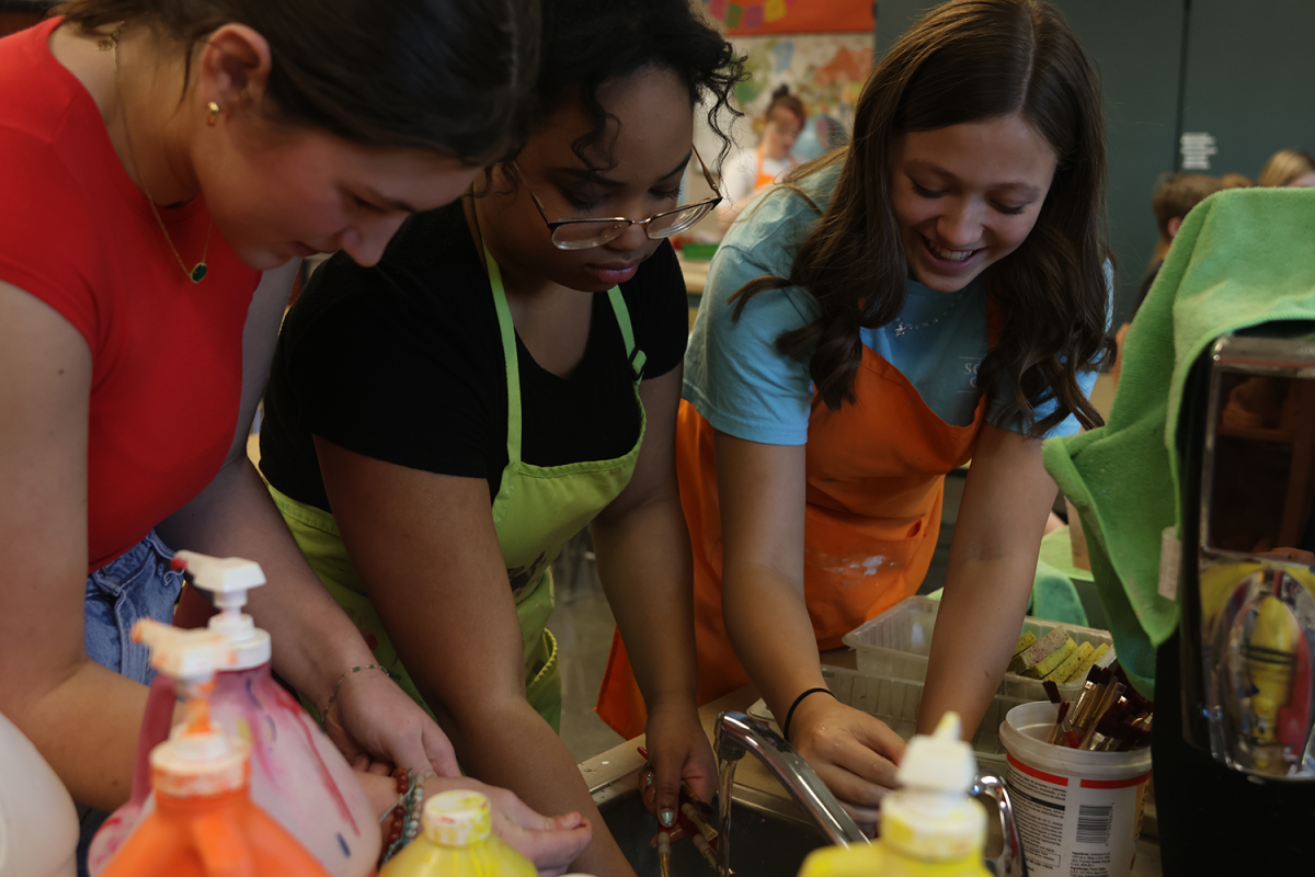 Smiling, juniors Lily Folendore and Autumn Graves help wash paint brushes alongside De Soto freshman Taryn Round.