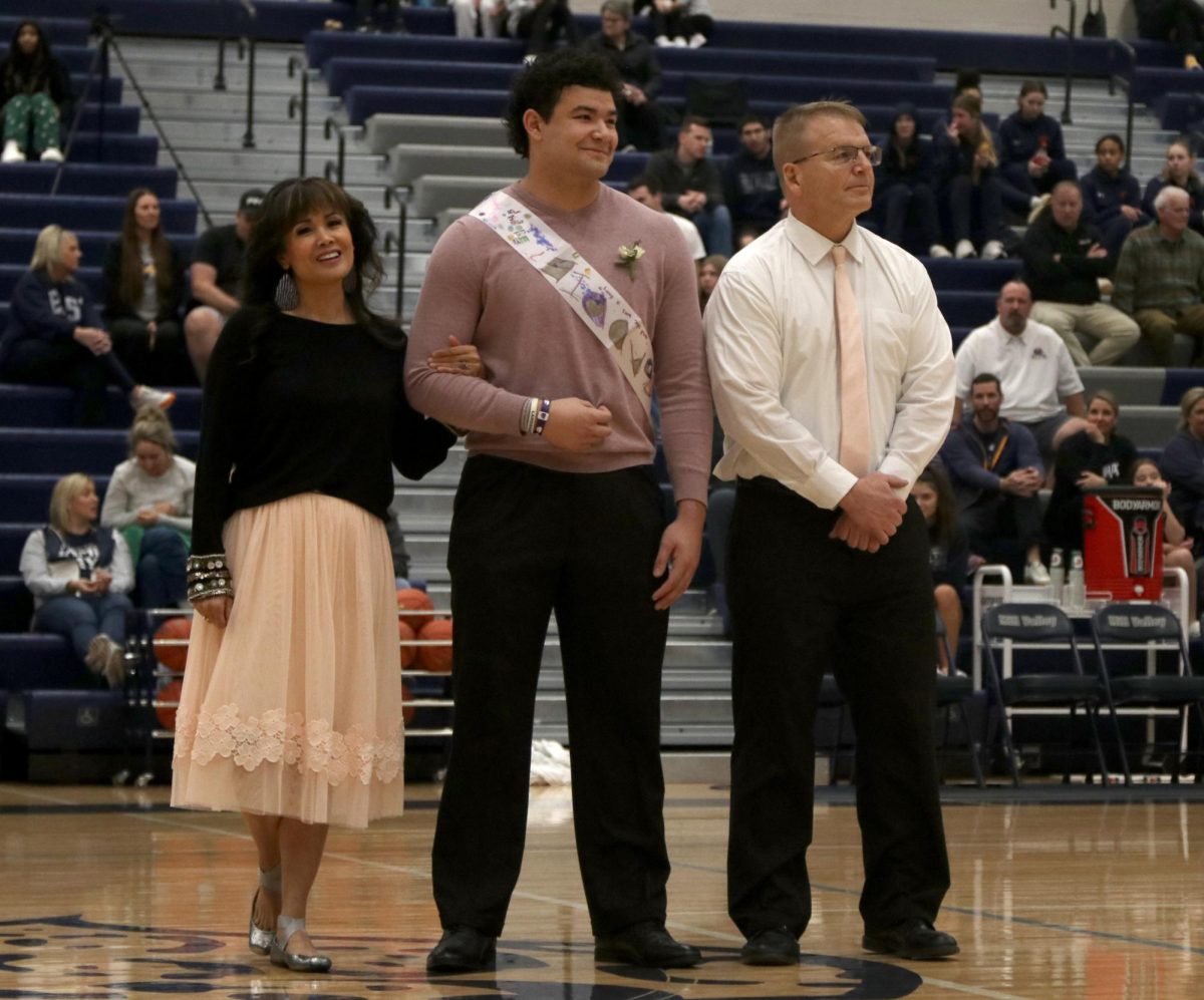 Smiling to the crowd, senior Truman Griffith stands next to his mom and dad, while being announced as a winter homecoming king candidate. 