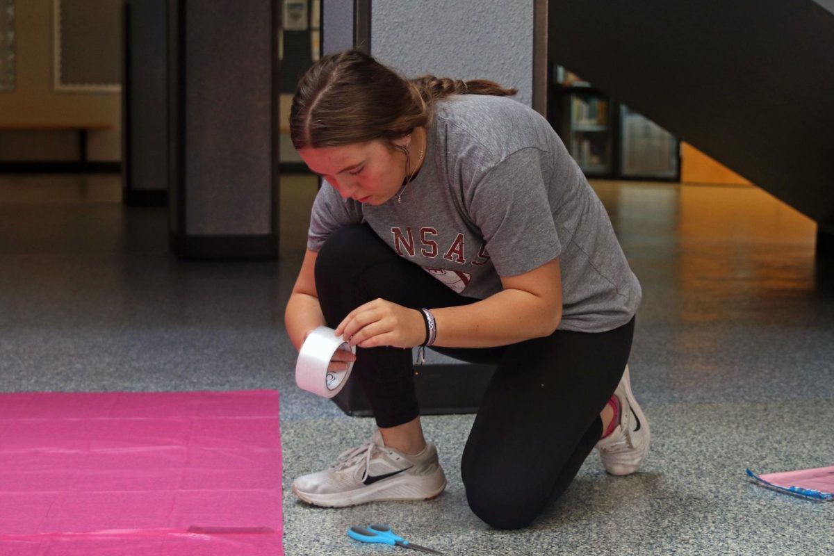 Down on one knee, senior Elly VanRheen gets tape for the poster. 