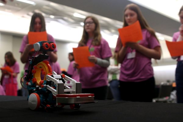 A tiny robot sits on the Computer Engineering table, demonstrating the wonders of computer engineering to several keen-eyed students. 