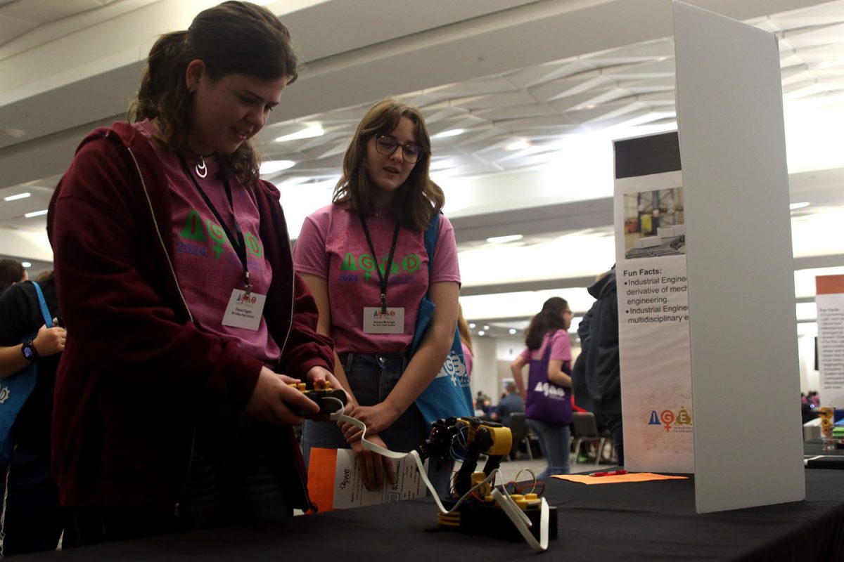 Using a controller, junior Elaina Fagen moves a small robot arm at the Industrial Engineering table.