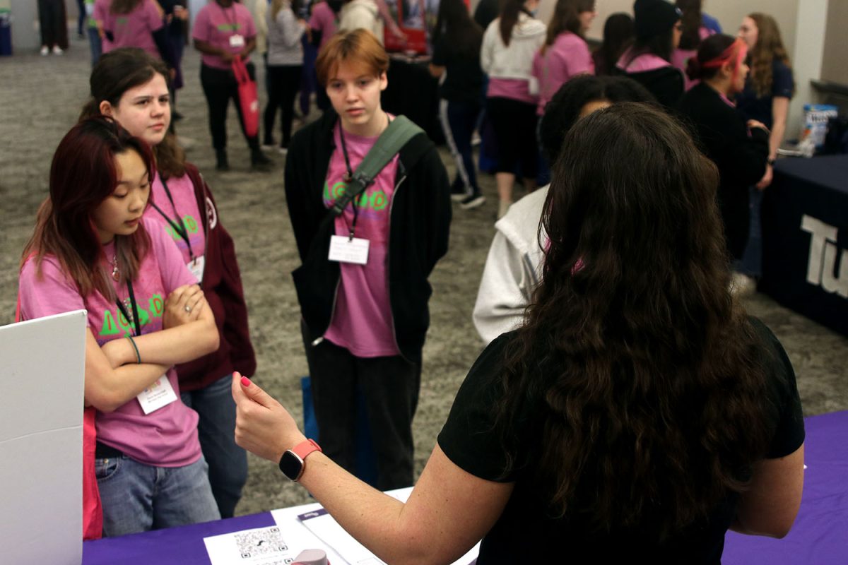 A representative from the international organization Society of Women Engineers (SWE) describes the role that SWE plays in womens lives across the globe to juniors Davin Bickerstaff, Elaina Fagen, and Cora Jones.
