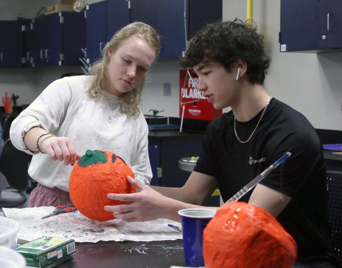 Getting help from art teacher Samantha MacAuley, junior Noah Pham wraps up his pumpkin painting project Thursday, Oct. 26. “I like having MacAuley as a teacher because she is very nice and helpful to the class,” Pham said. “She lets us have our own freedom with projects so that we can have fun.”