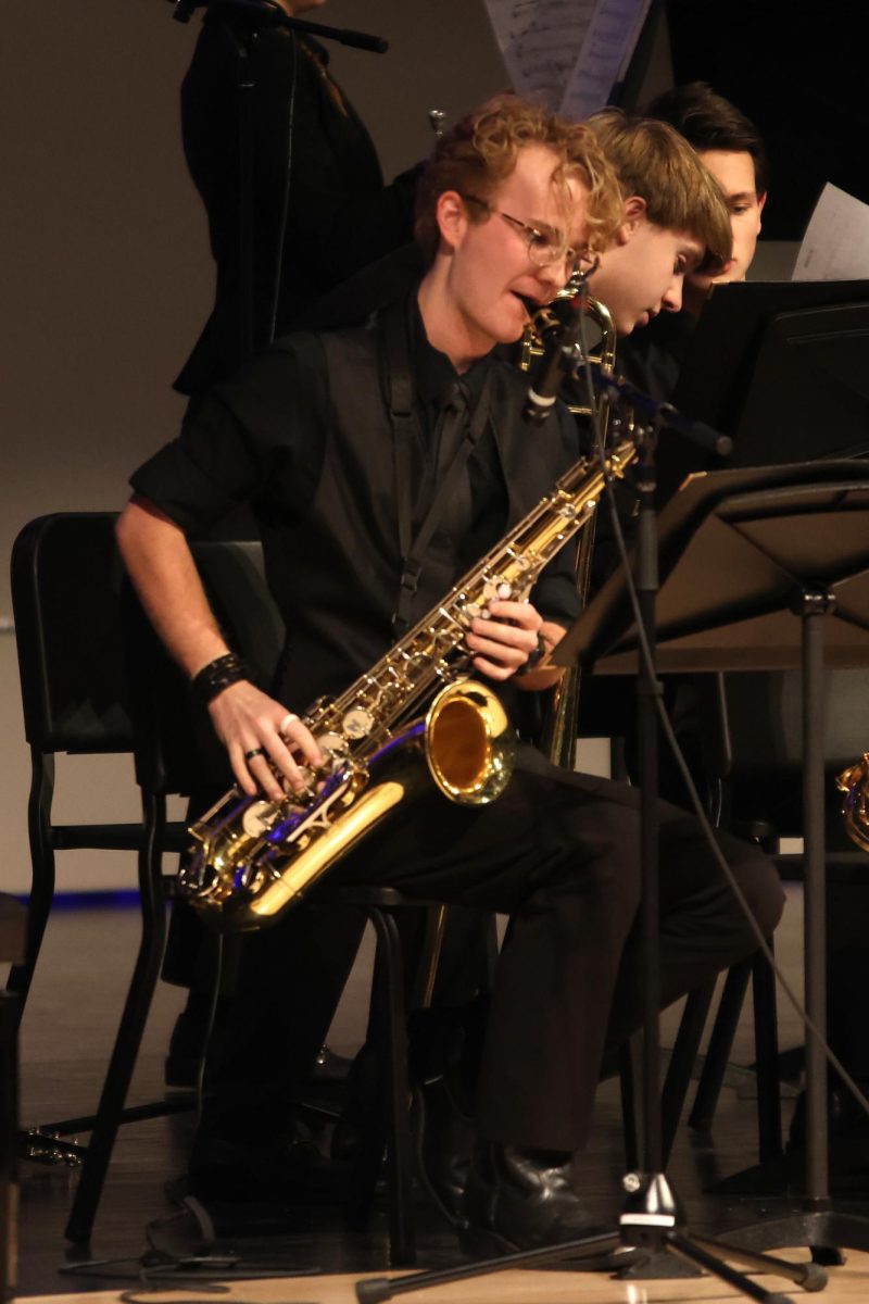 Looking down at the music sheet, senior Evan Mack plays his saxophone.