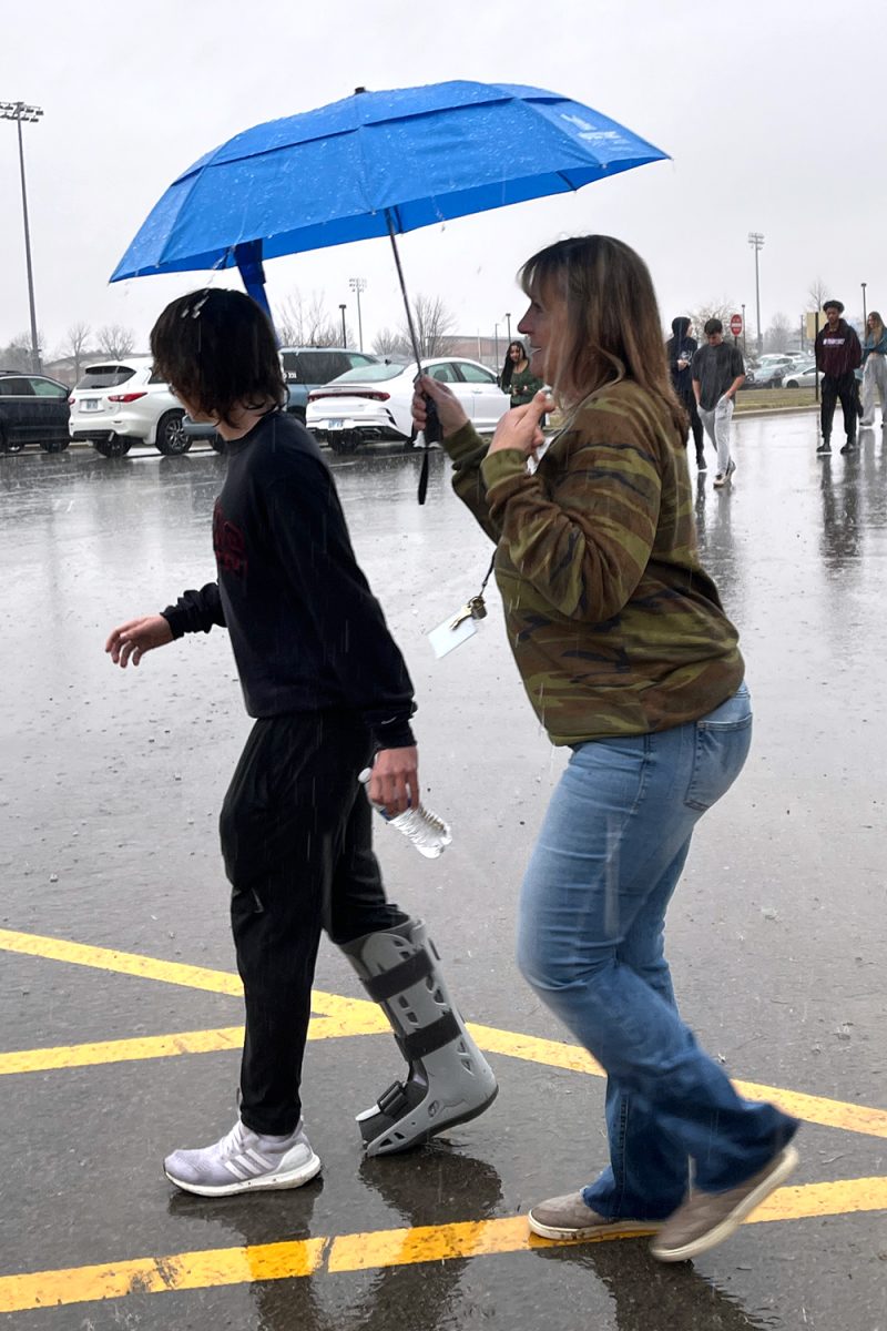 Holding up an umbrella, registrar Deana Thom blocks junior Thomas Helms medical CAM boot from the rain.