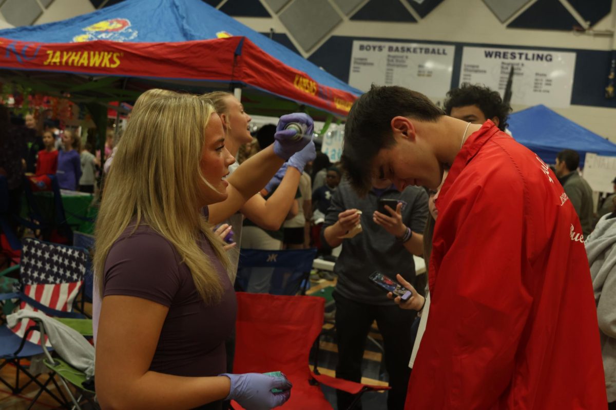 Senior Trinity Baker sprays senior Kenten Laughman’s hair green at the Fighting Fashionistas station. 
