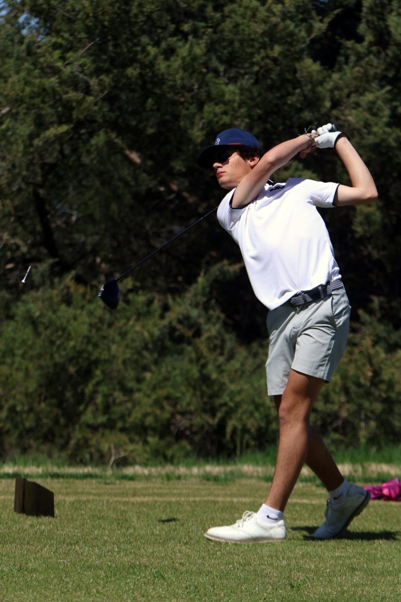 Holding his club up, junior Brett Spandet  focuses on his recently hit ball. 