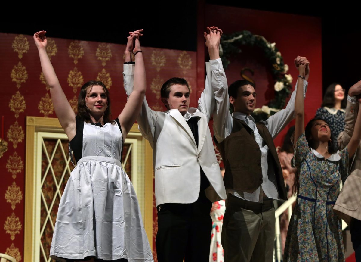 Looking out at the audience during the curtain call, sophomores Lillian Schleicher and Nathaniel Petrowsky and junior Zach Casper hold their hands in the air after bowing. 