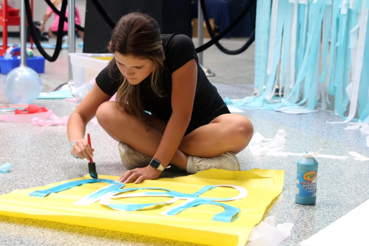 Sponge in hand, senior Brynn Shideler paints a “Mamma Mia!” themed sign. 