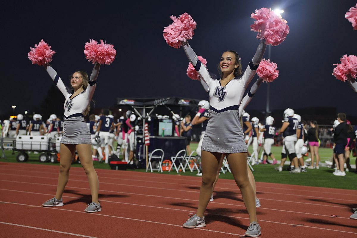 Smiling, senior Josie Mason waves her pom poms in the air.