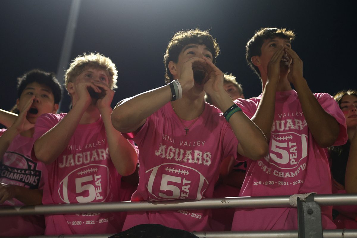 Hands to his face, senior Noah Pham cheers for the football team with his friends. 