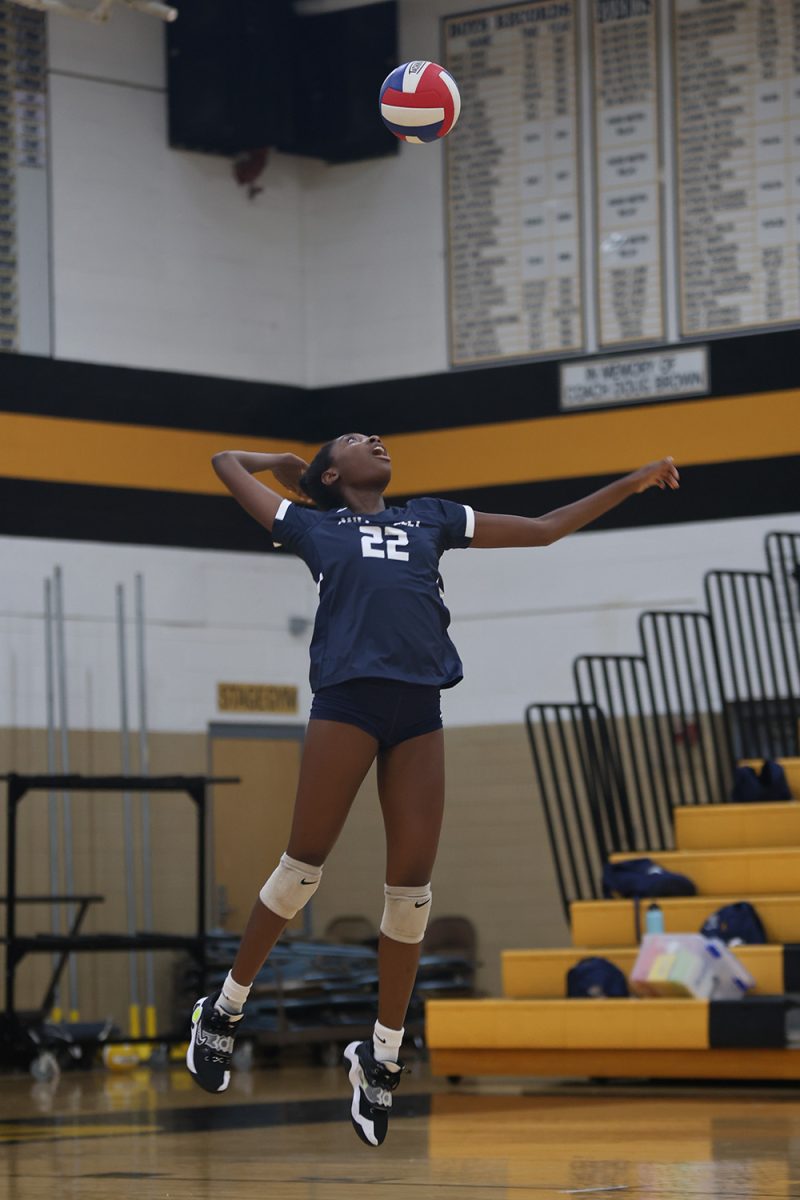 In mid-air, junior Olivia Nzioki pulls back her arm to serve the ball Thursday, Oct 3. 