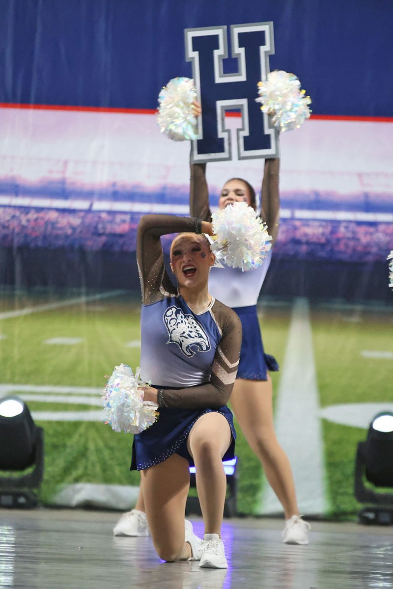 On one knee, senior Ashley Ayers poses with her pom poms framing her face.