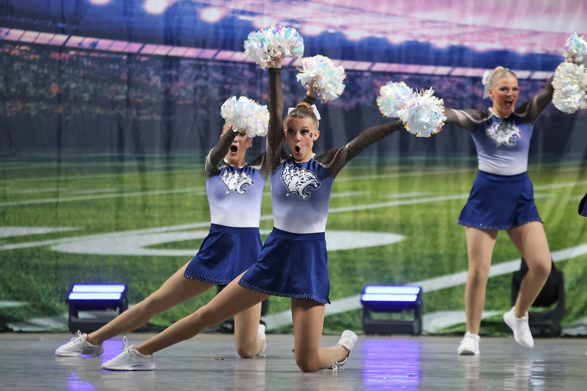 With one leg out, junior Ella Jones dances and holds her poms in the air. 