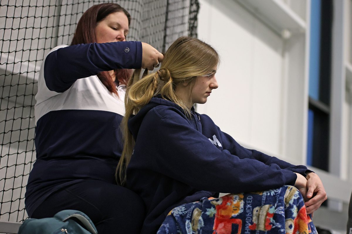 Wrapped in a blanket, junior Finley Rose gets help from her coach to put her hair in braids.