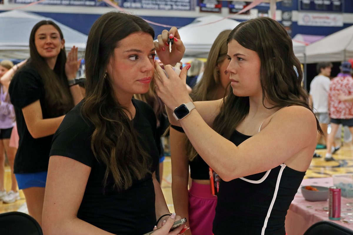 Junior Kyndal Geis applies face paint on senior Riley Maguire. 
