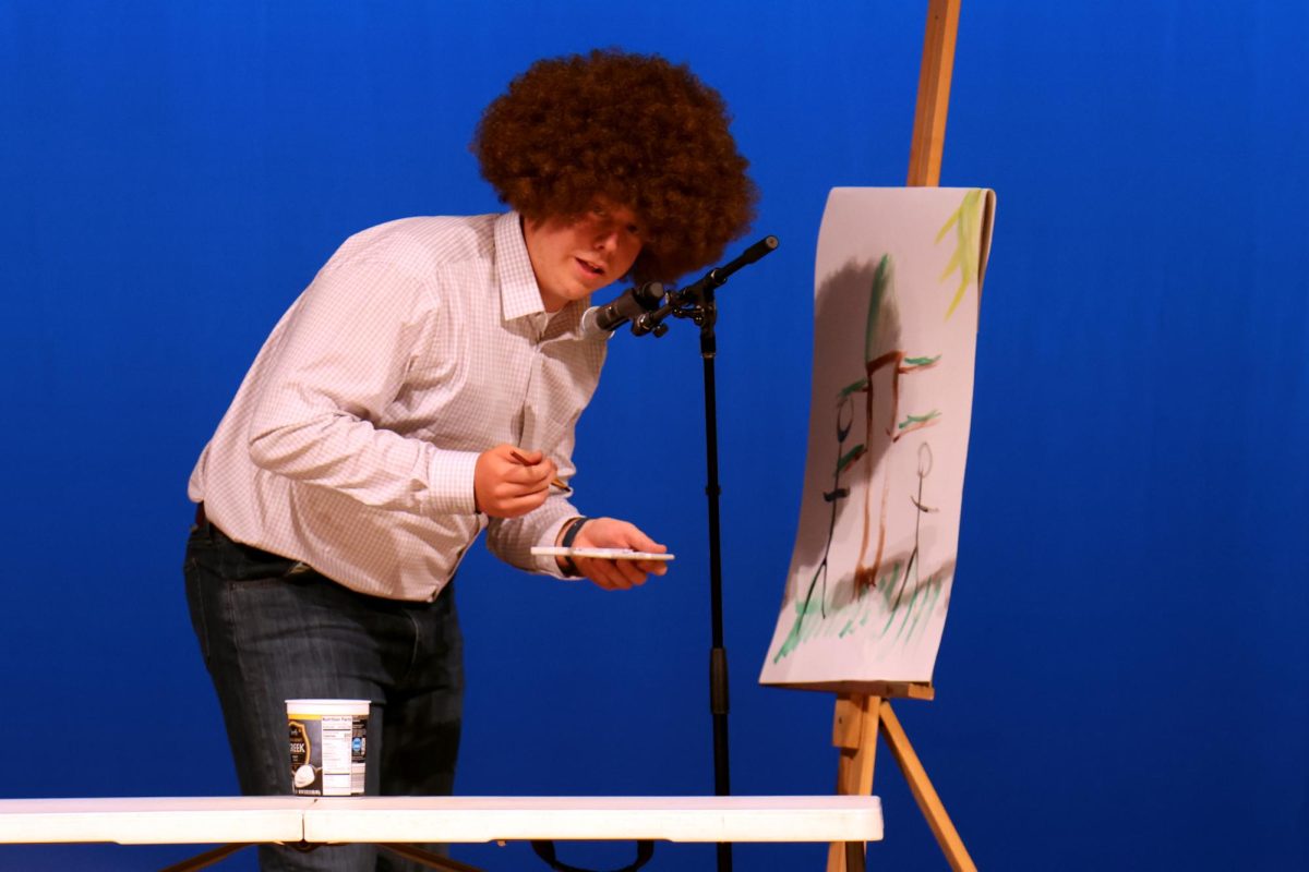 Speaking into the microphone, senior Aiden Lehr paints a Bob Ross painting as his talent.
