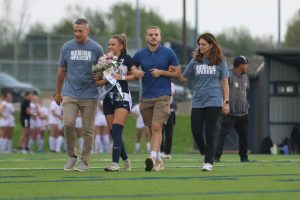 Senior Marissa Hoelting walks down the field with her family as the crowd applauds her.