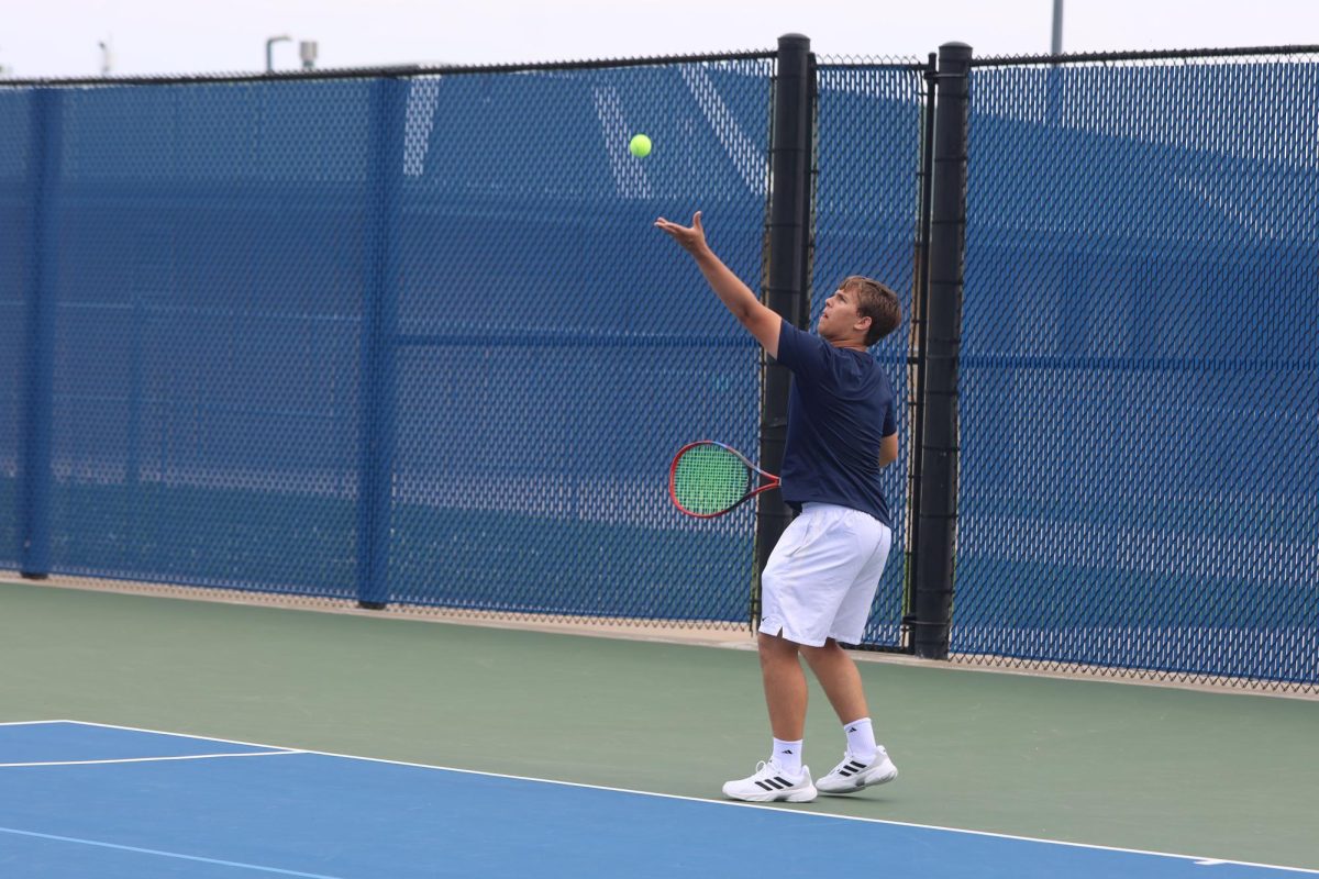 Racket in the air, junior Jack Thomas serves the ball to the opposing team.