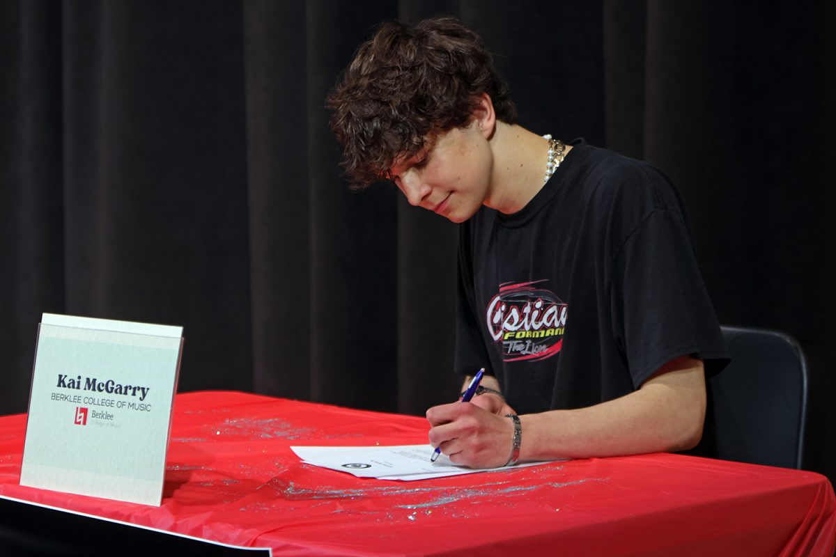 Smiling, senior Kai McGarry signs his letter. 