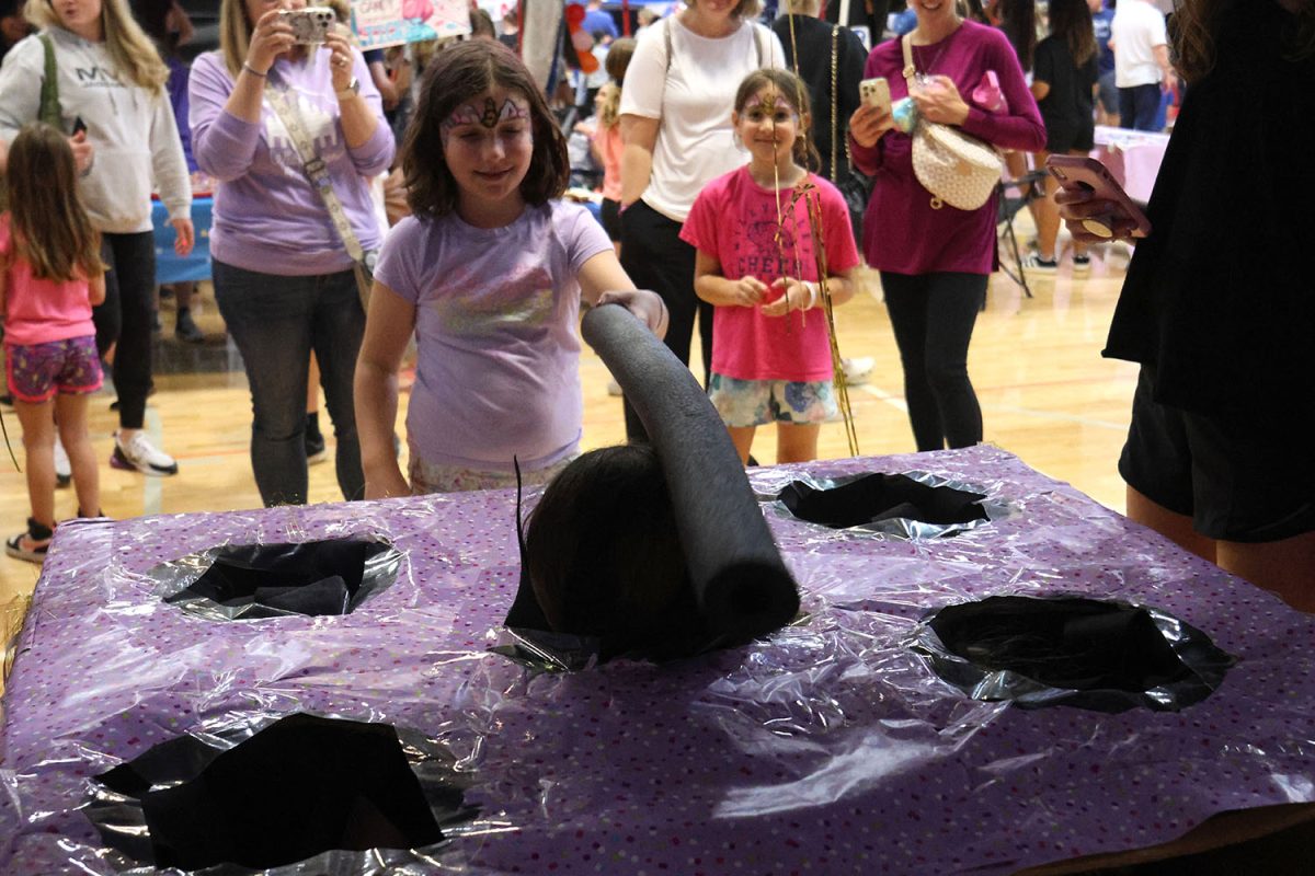 Wearing her face paint, a kid enjoys playing whack-a-mole at Relay For Life. 