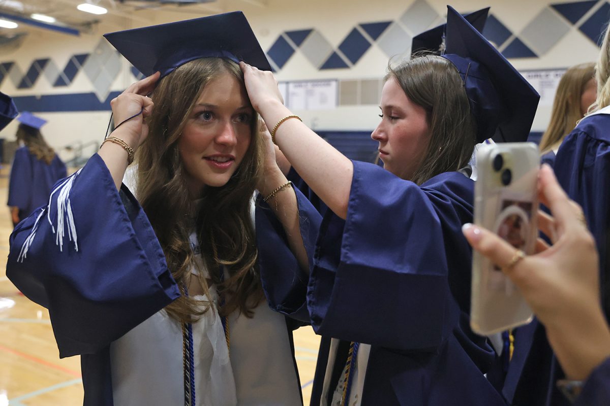 Senior Gracie Kurzejeski gets assistance from senior Reese Miller in getting her cap on while another friend holds up the selfie camera. 