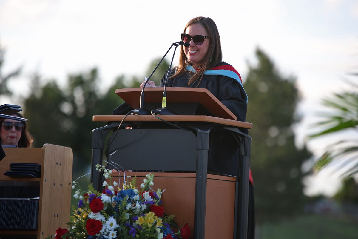 Smiling, history teacher Angie Dalbello reads aloud names while the seniors walk across the stage.