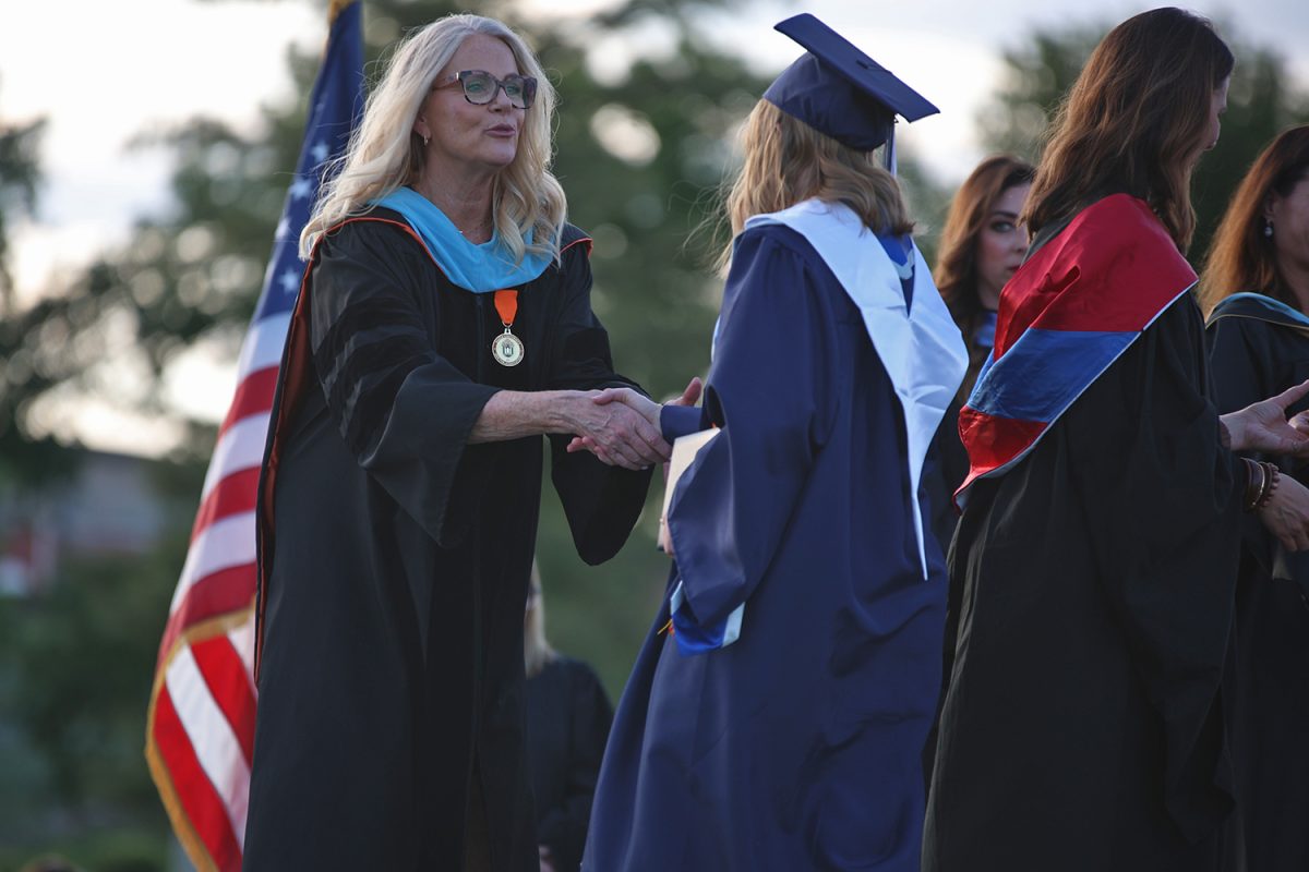Principal Dr. Gail Holder shakes the hand of a graduate while on stage.