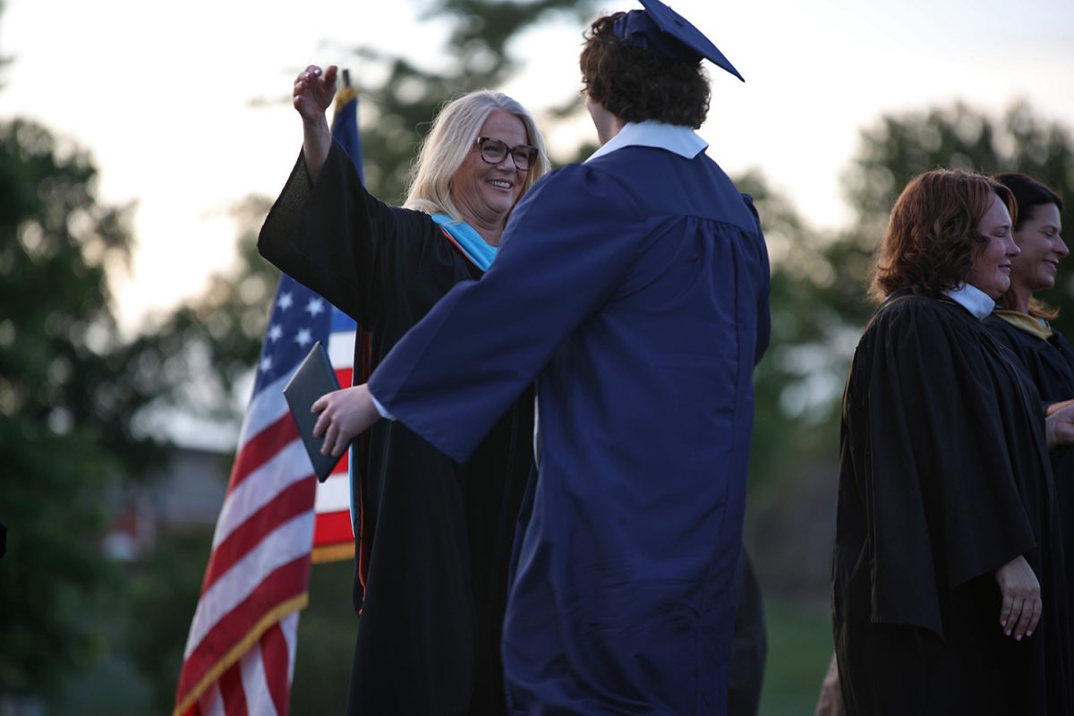 Grinning, principal Gail Holder opens her arms to hug a graduate after they receive their diploma.