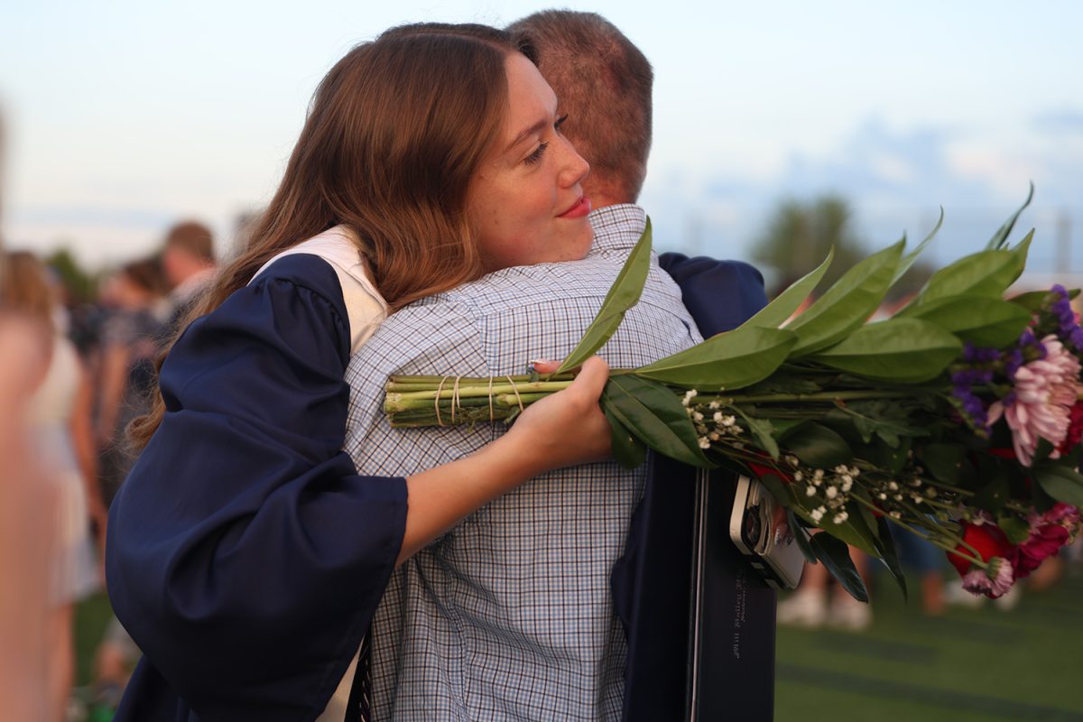 With the sun setting, senior Elise Davis hugs a family member with flowers in her hand. 