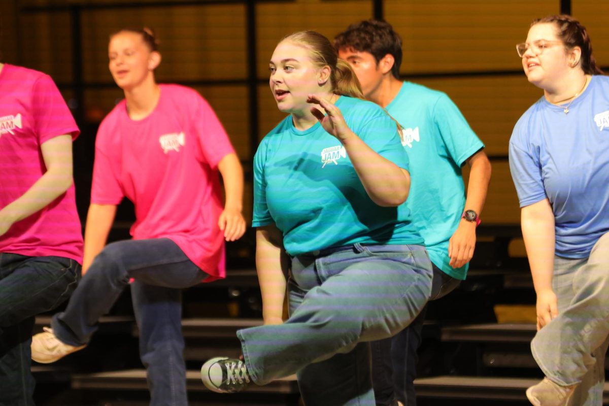 Leg lifted, senior Lillian Schleicher holds her ankle while singing to the crowd.