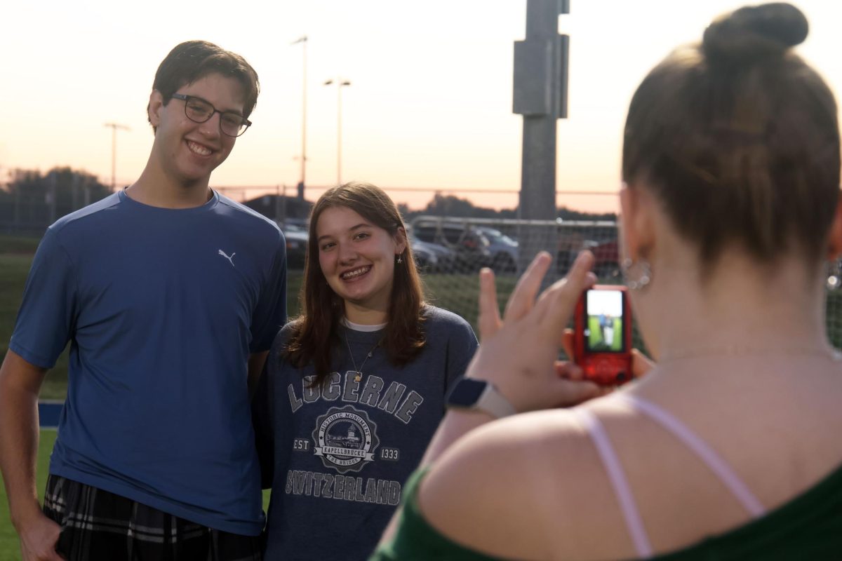 Seniors Barron Fox and Hannah Stephensen stand in front of the sunrise as senior Izzy Simms photographs them.