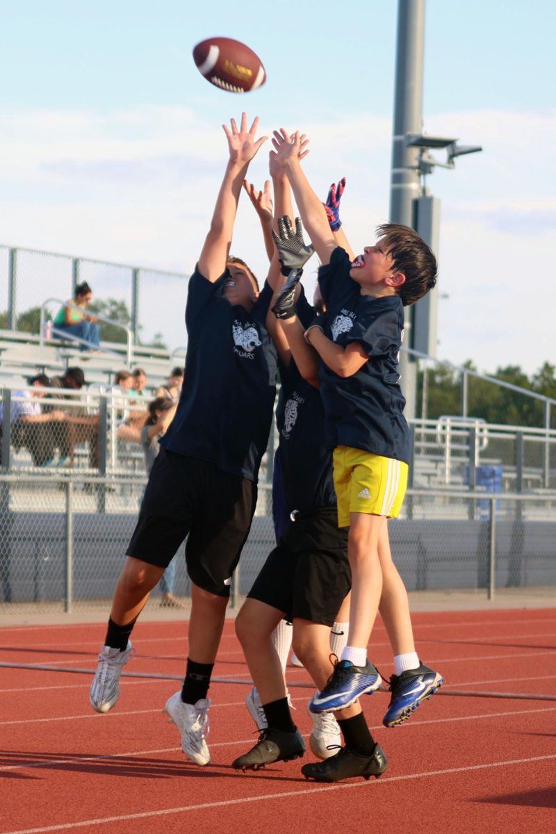 Hands reaching up, Junior Jag football players play catch on the track after their scrimmage.
