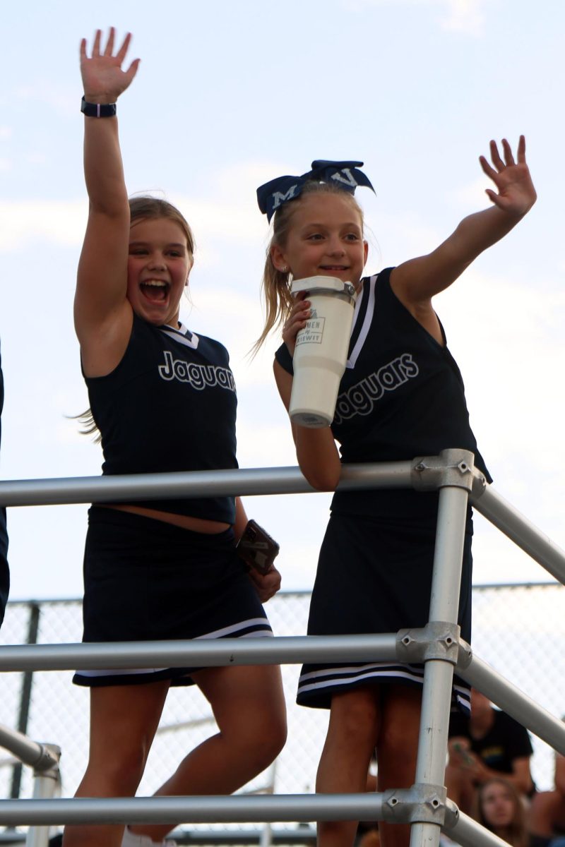 Smiling, junior jags wave to the high school cheer team from the stands. 