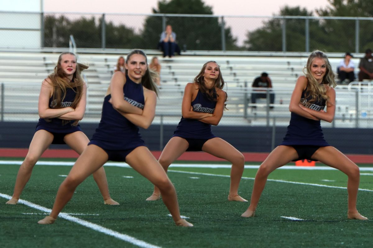 Arms crossed, juniors Chloe Thomas and Maddie Lawson and Seniors Addison Maier and Bailey Bret lean side to side before the high school scrimmage. 