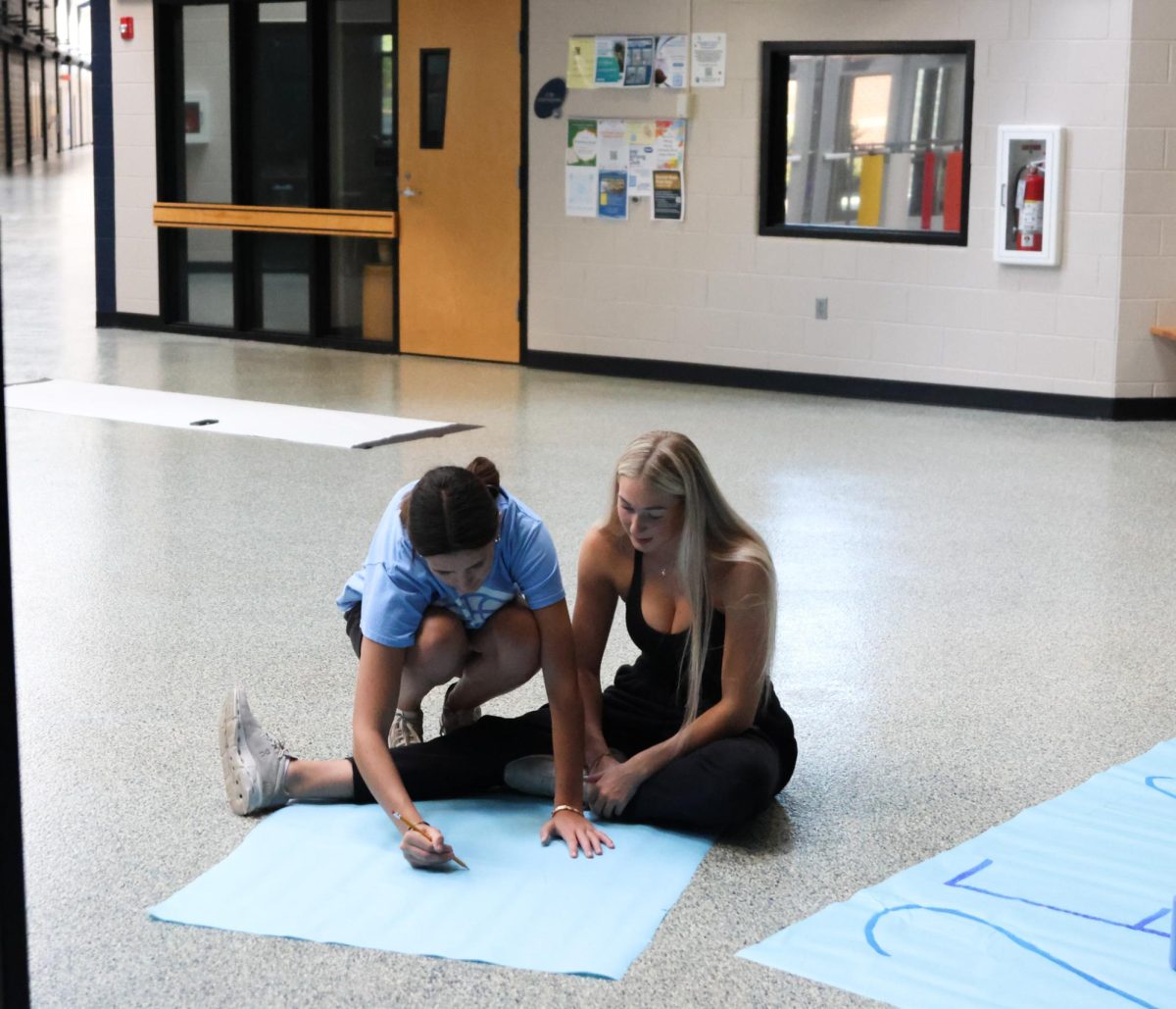 Seniors Paige Roth and Callaway Clifton work together to decorate the senior sign