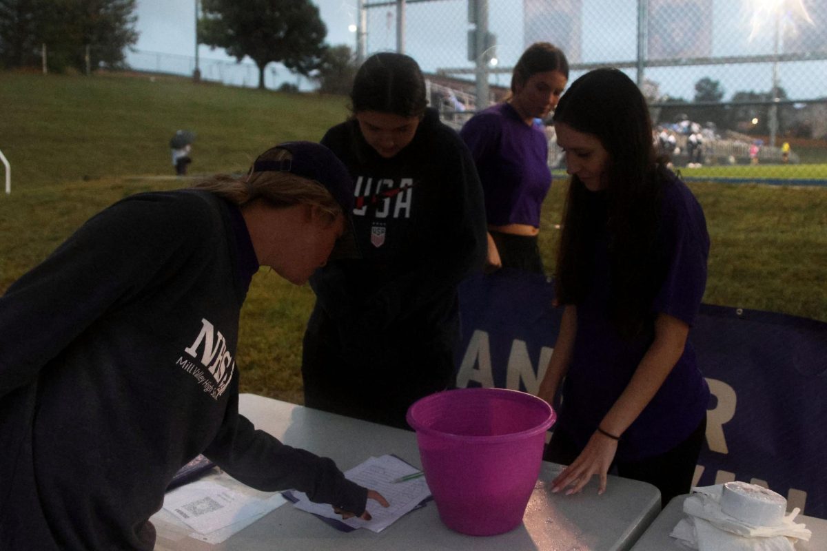 While selling rubber ducks and donuts at the entrance to the RFL Purple Out varsity soccer game, sophomore Nora Claycamp and junior Kady Coulibaly go through the list of rubber duck sales with  Relay for Life sponsor Kirsten Jones, Tuesday, Sept. 23.