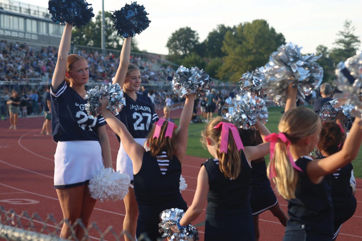 Arms raised juniors Annie Bohon and Kenna Long practice cheers with their group of Junior Jags during Night Lights, Thursday, Aug. 28. During Night Lights high school cheerleaders help younger cheerleaders to cheer during the scrimmages for the Junior Jag football teams. 