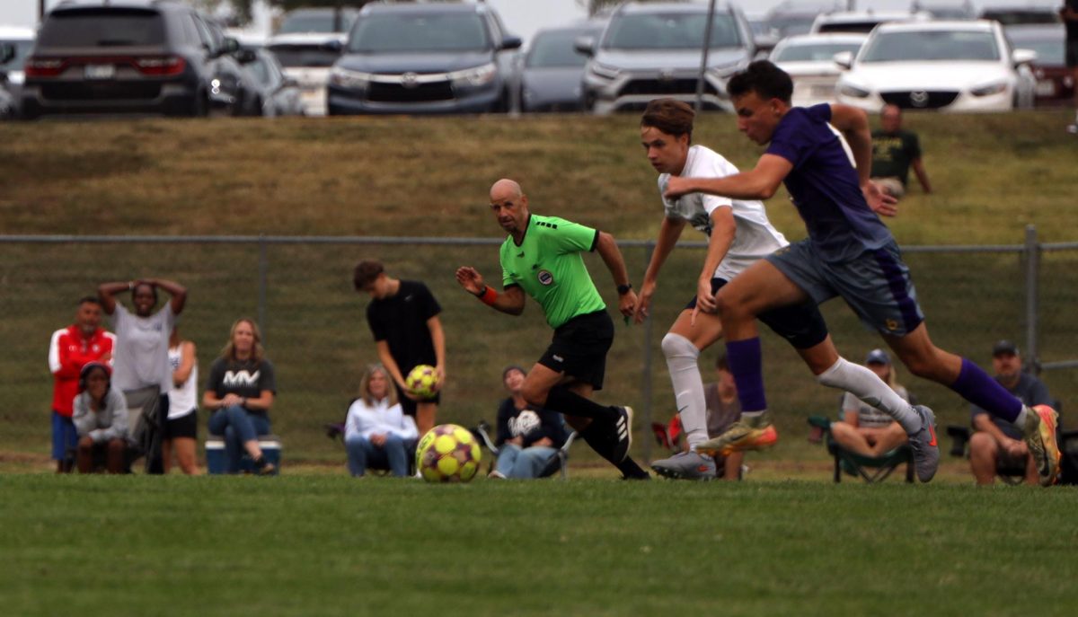 The players run for the ball with the ref keeping a close eye. 