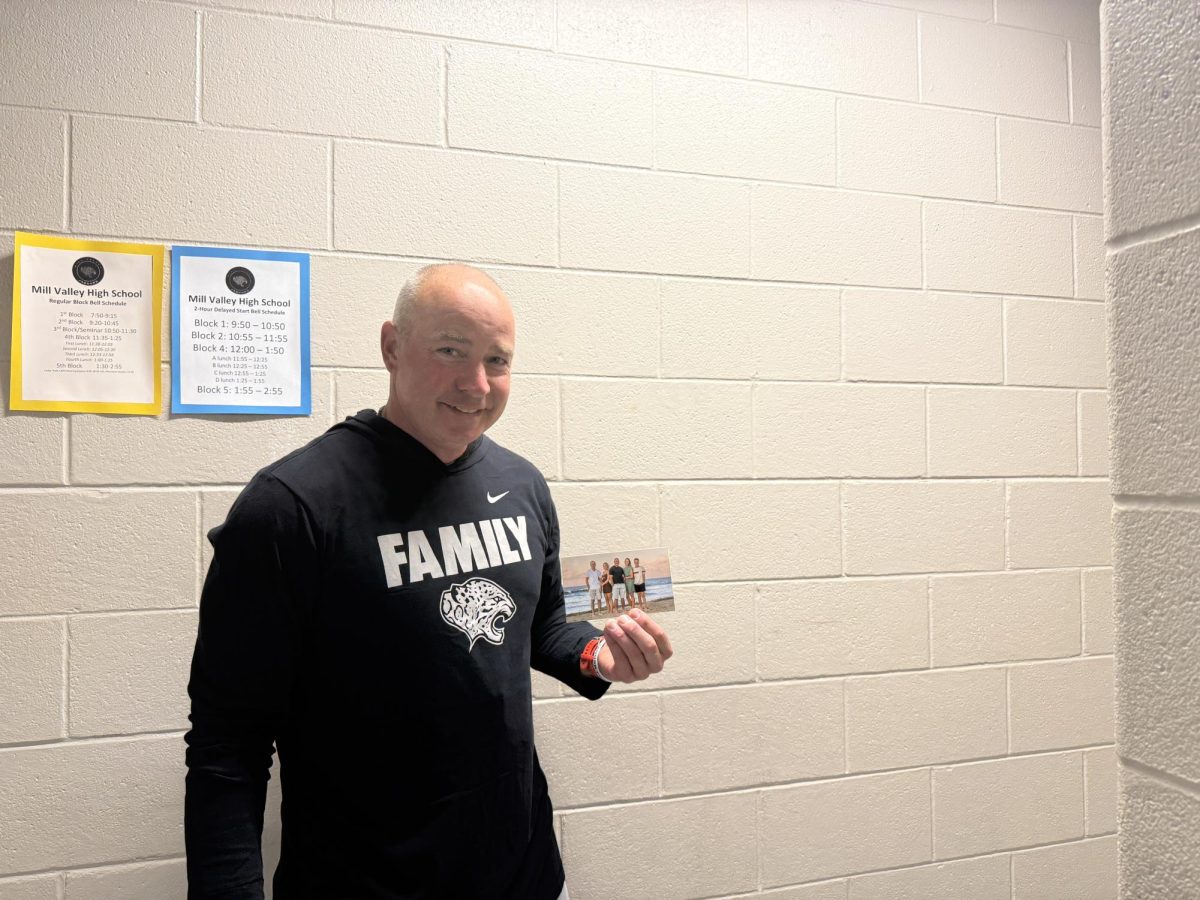 P.E. teacher Larry Benson smiles with a picture of his family, the photo is an important item he enjoys keeping at his desk. 