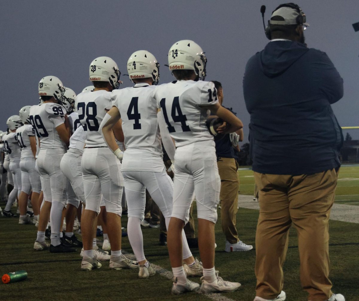 Coach Paul Gilmore stands beside the players on the sidelines.