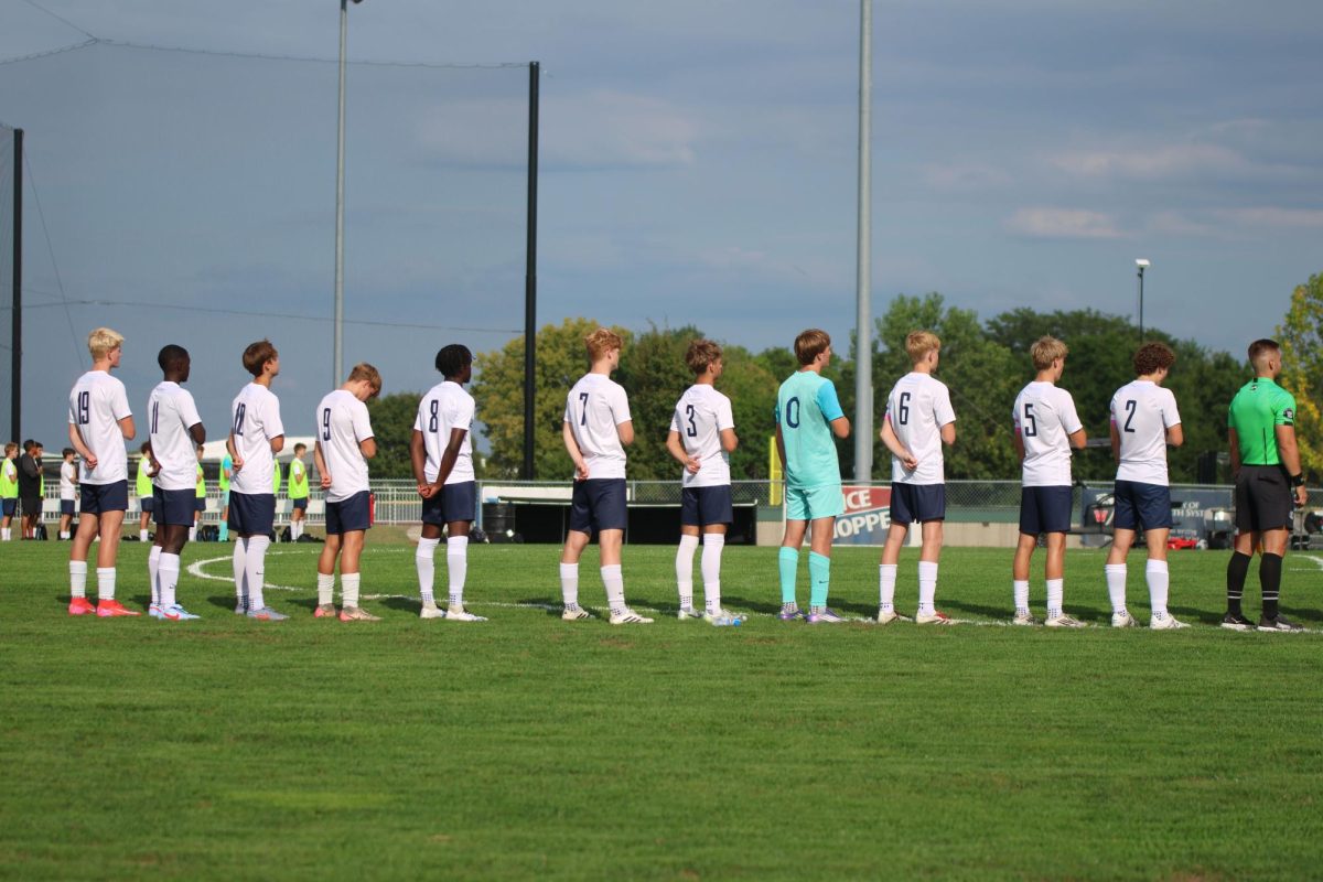 Varsity boys soccer players put their right hands over heart and look at the flag for the national anthem. 