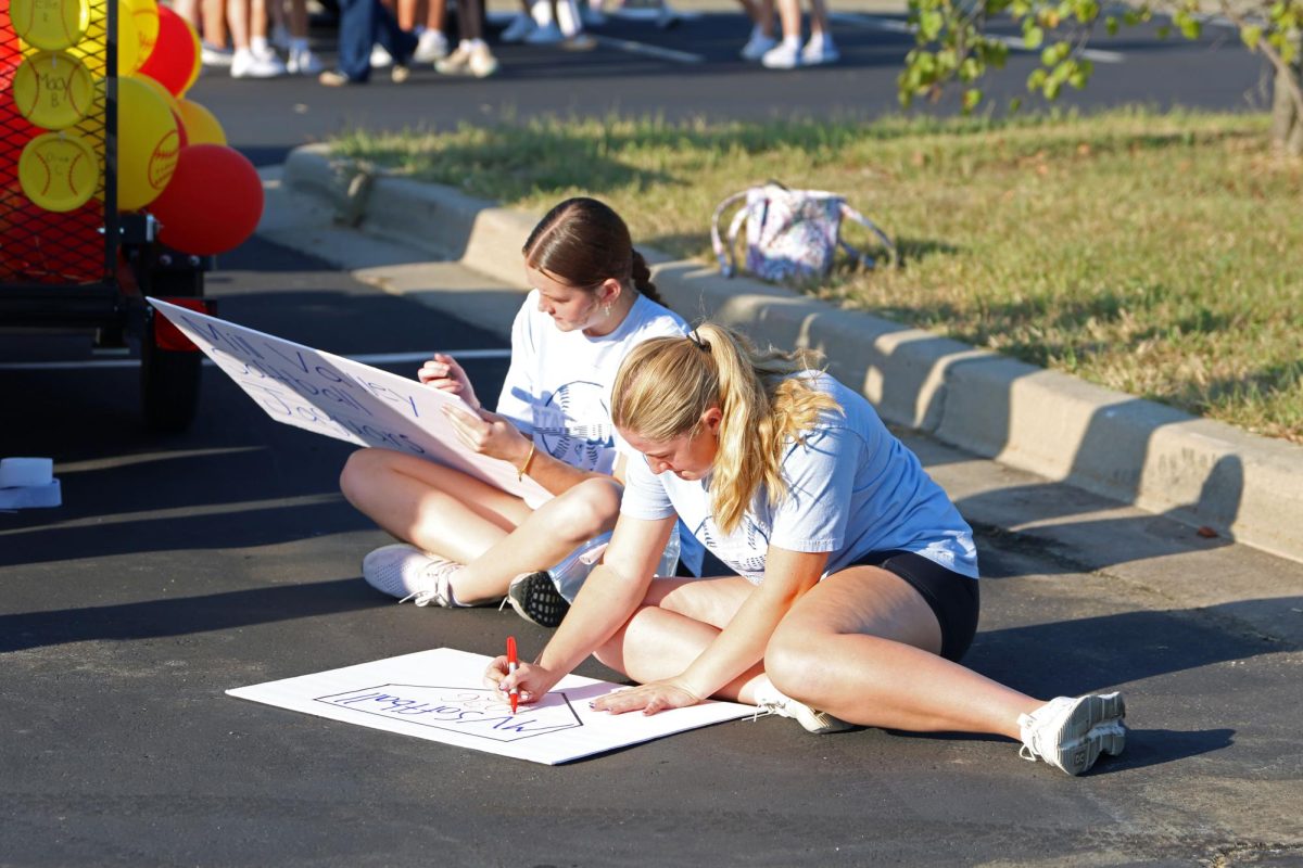 Senior Macy Brunner and junior Addy Moeller create signs for the softball float.