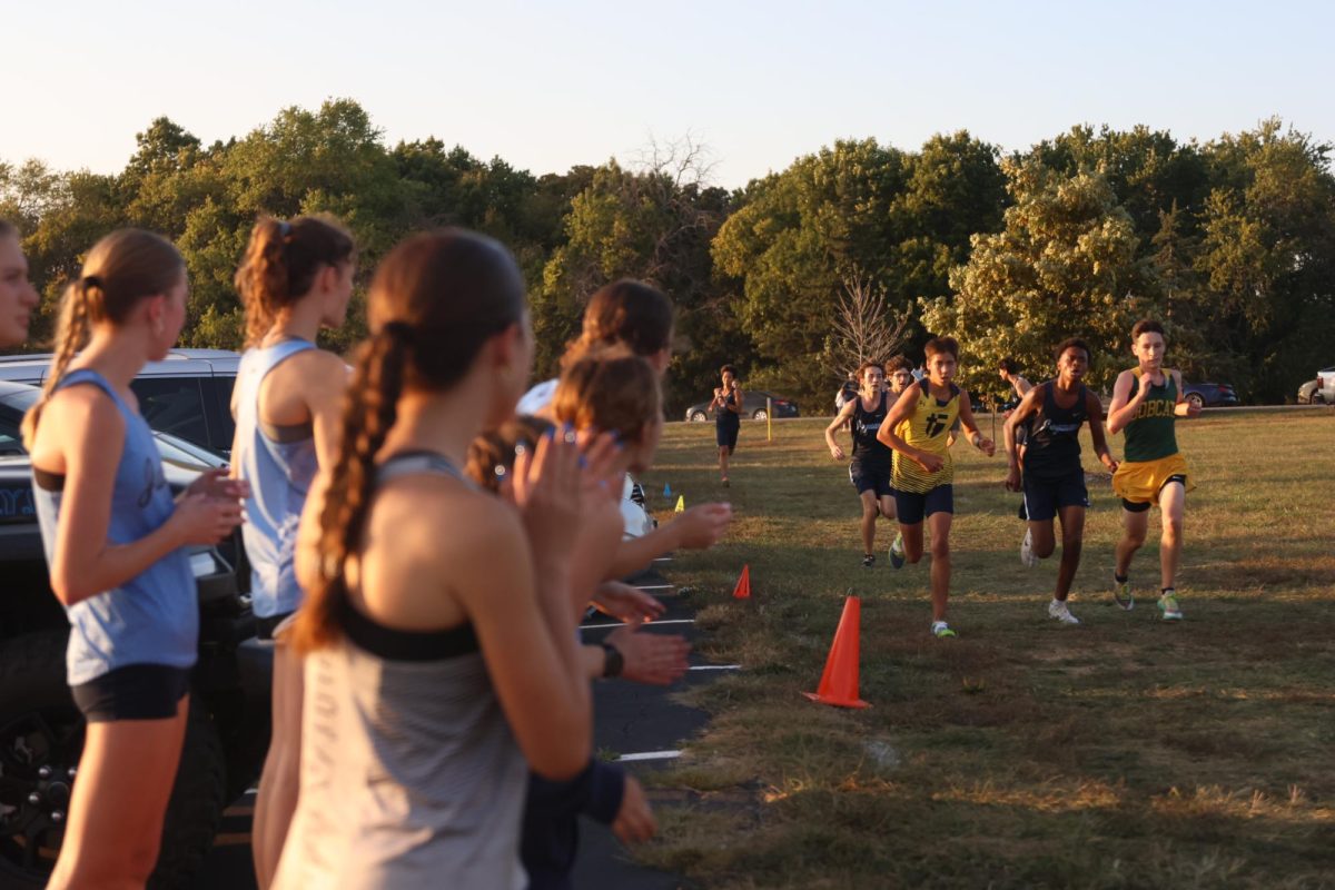 The girls’ varsity team cheers on senior Carson Curry and sophomore Gabe Muttai as they stride to the finish.