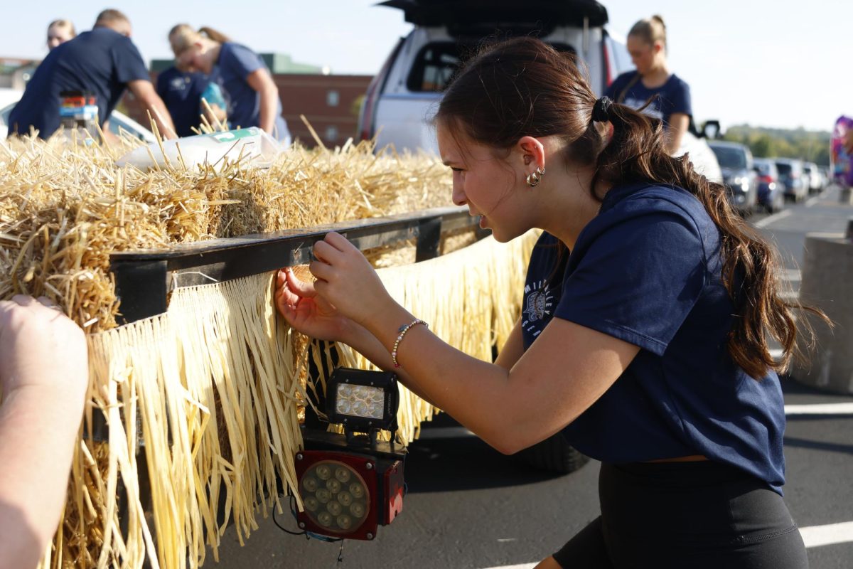 Preparing for the Homecoming Parade on Oct 1, 2025, Junior Charli Redden decorates the soccer team's float with a straw fringe. 