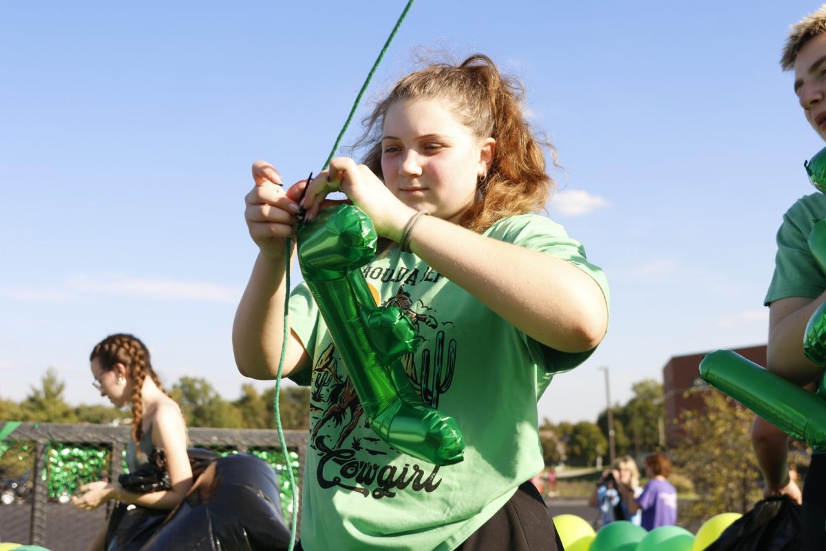 Sophomore Ava Munsey ties balloons to the class float before the homecoming parade on Oct 1, 2025. 
