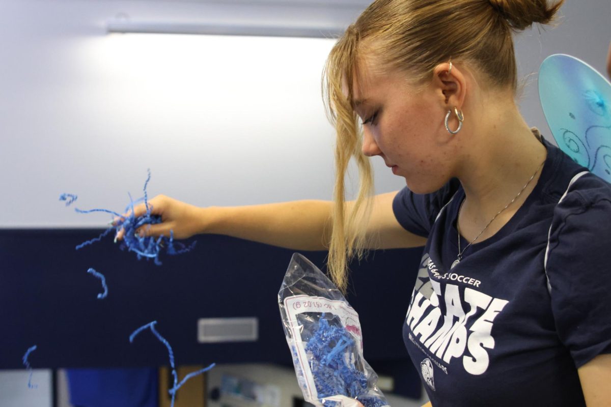 With blue butterfly wings, senior Taylor Goodwin sprinkles blue paper over the floor. 

