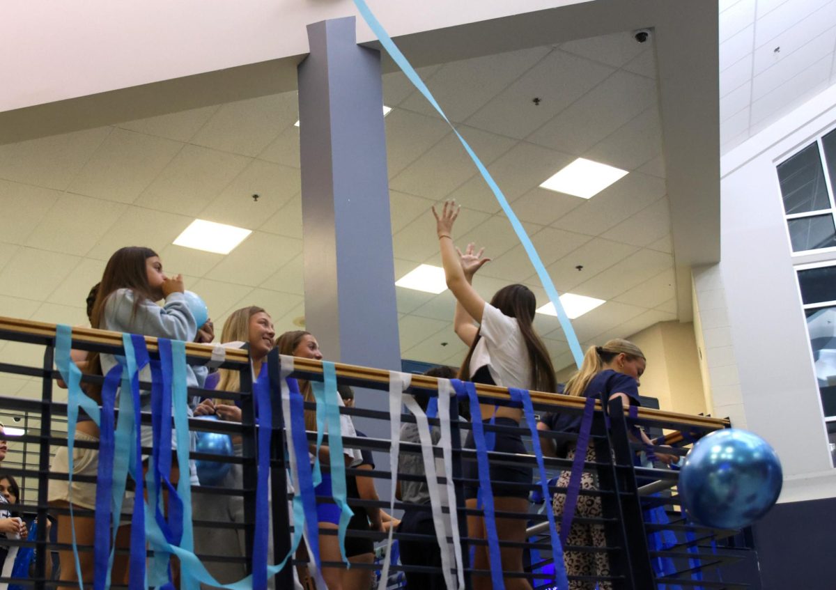 Standing on the stair landing, senior girls throw streamers up in the air. 