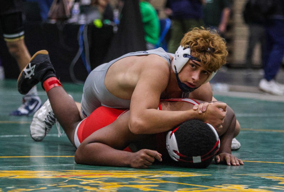 Looking to his coaches for advice, junior Quinn Vaka pauses with his opponent pinned on his stomach.