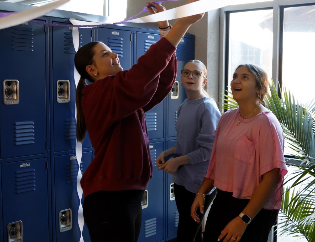 Hanging streamers, sophomores Nora Claycamp, Maddy Sprecker and Quinn Slattery decorate lockers for Purple Bomb.